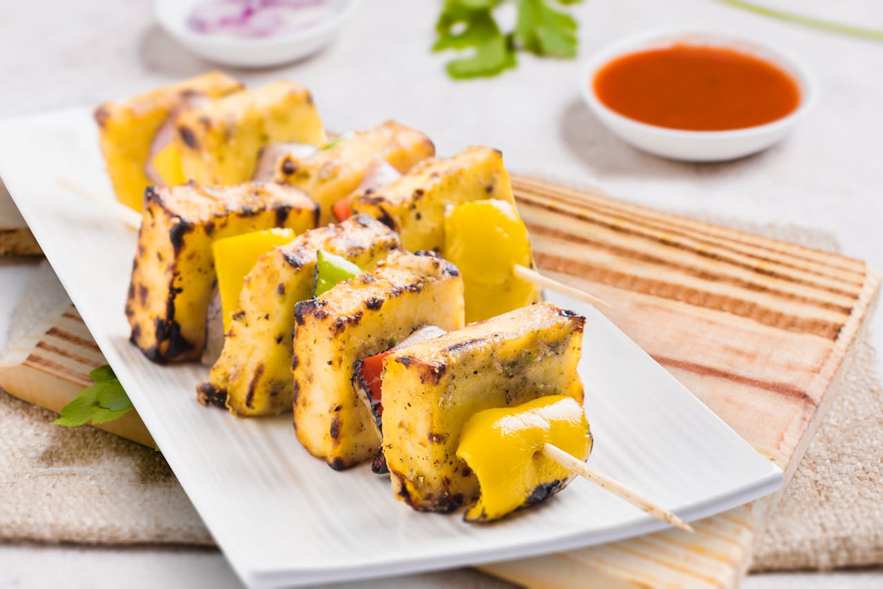 Tasty grilled paneer tikka skewers served on a plate with sauces, perfect for an Indian cuisine experience.